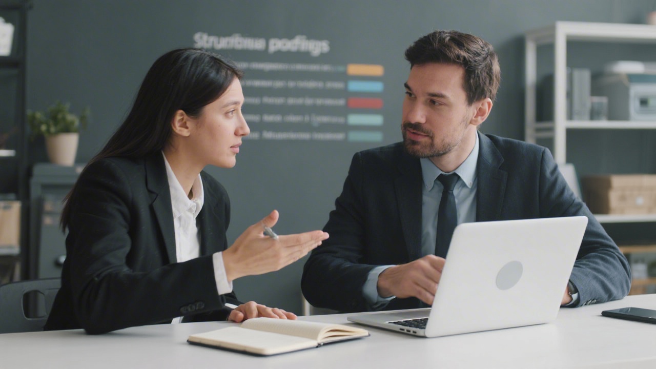 Two professionals discussing marketing objectives over a laptop and notebook, emphasizing a structured onboarding process for new clients.